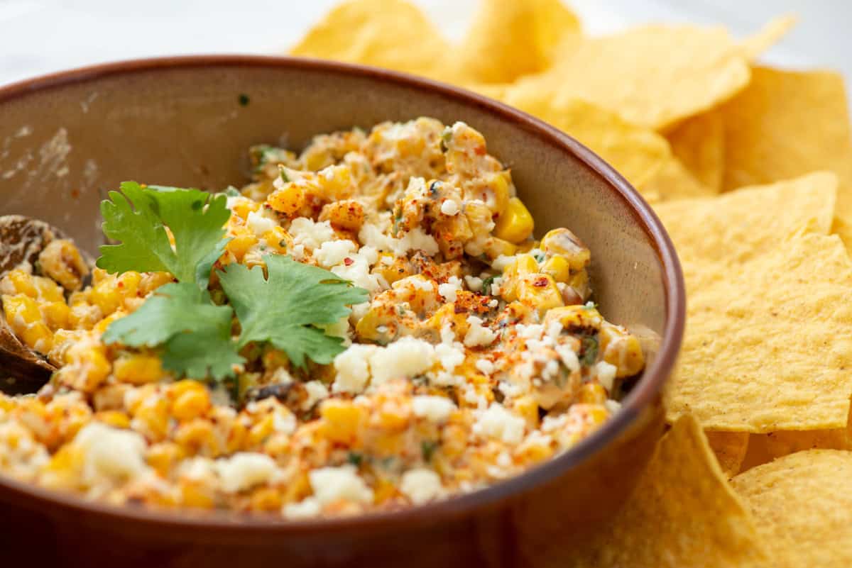 Bowl of Mexican Street Corn dip garnished with cilantro next to tortilla chips
