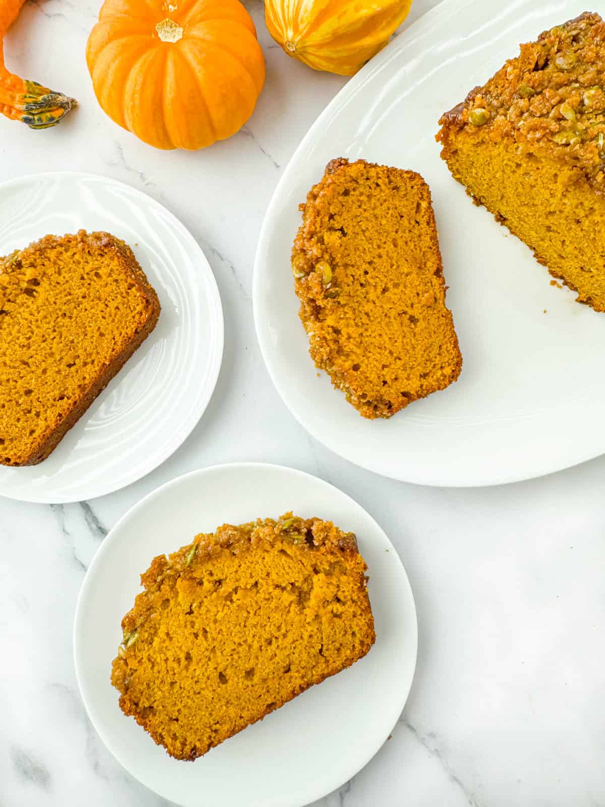 Multiple slices of pumpkin bread with streusel topping on multiple plates