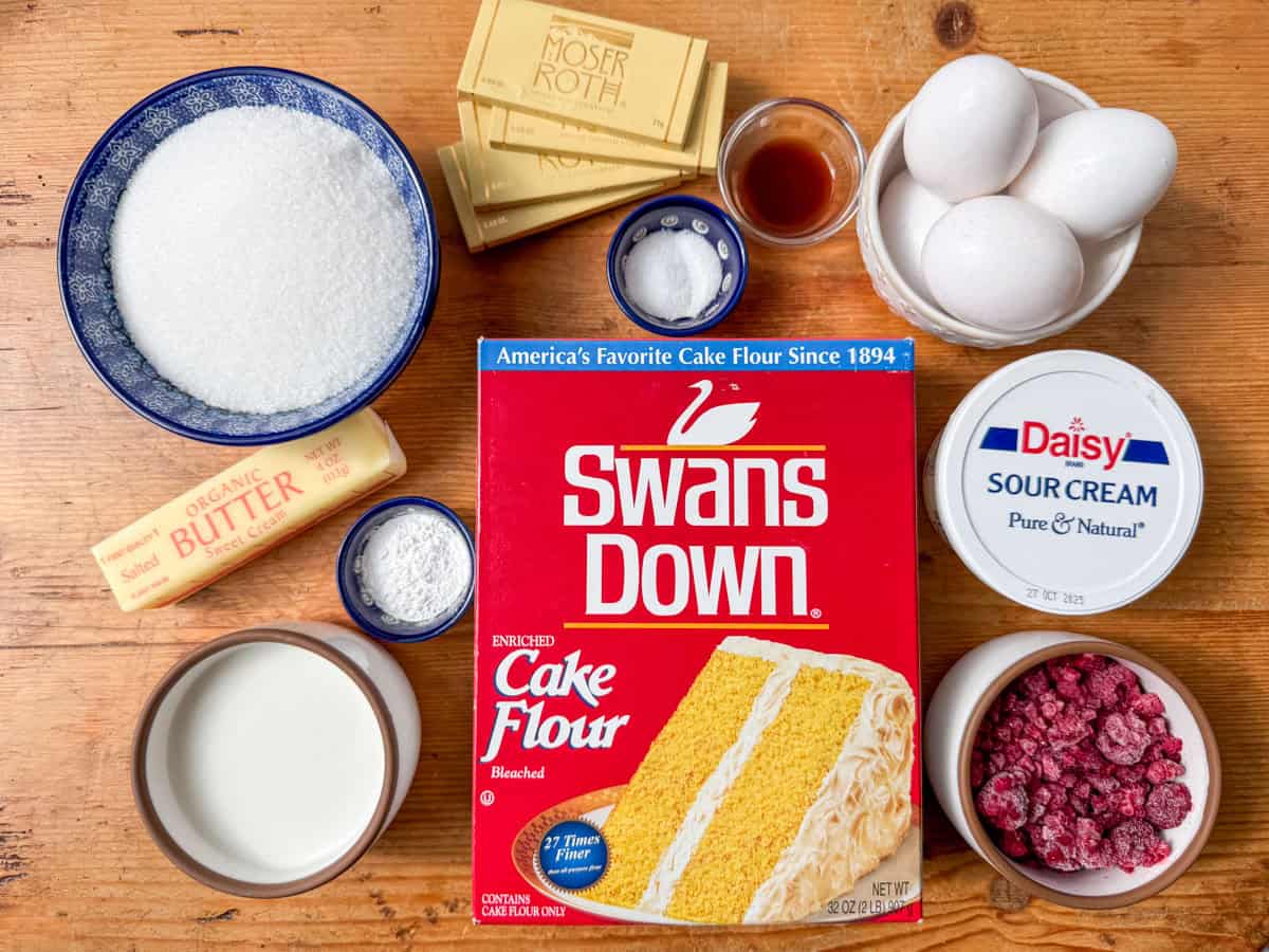 Ingredients needed to make white chocolate raspberry bundt cake: cake flour, white sugar, milk, sour cream, eggs, frozen raspberries, white chocolate, salted butter, baking powder, vanilla, salt.