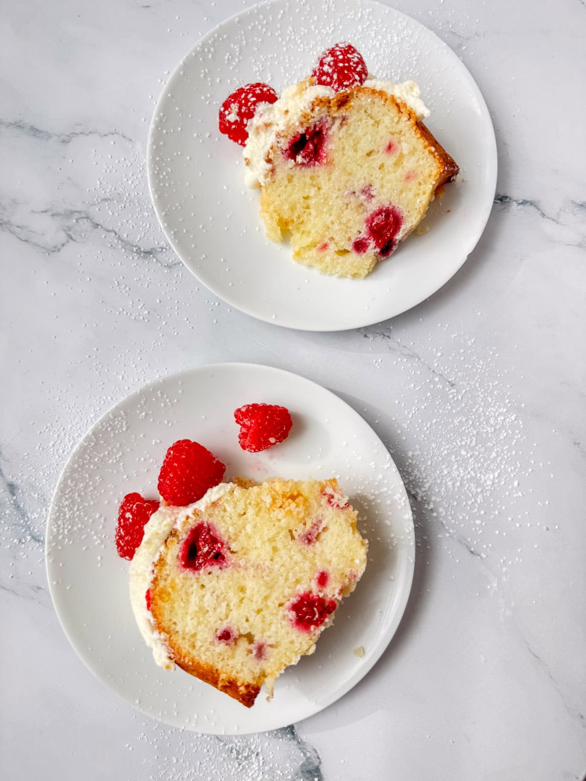 An overhead view of two plates, each with a slice of white chocolate raspberry bundt cake