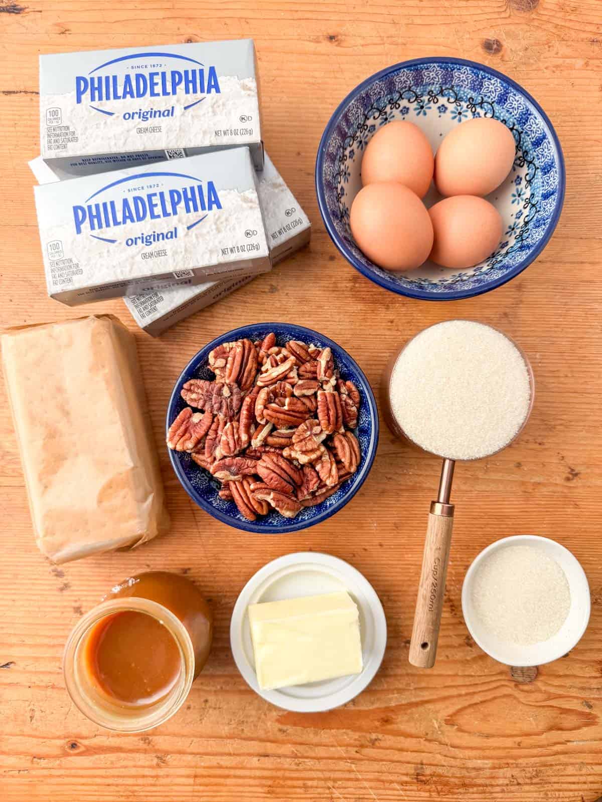 Ingredients needed to make a salted caramel pecan cheesecake: pecans, graham crackers, salted butter, cream cheese, white sugar, eggs and salted caramel sauce.