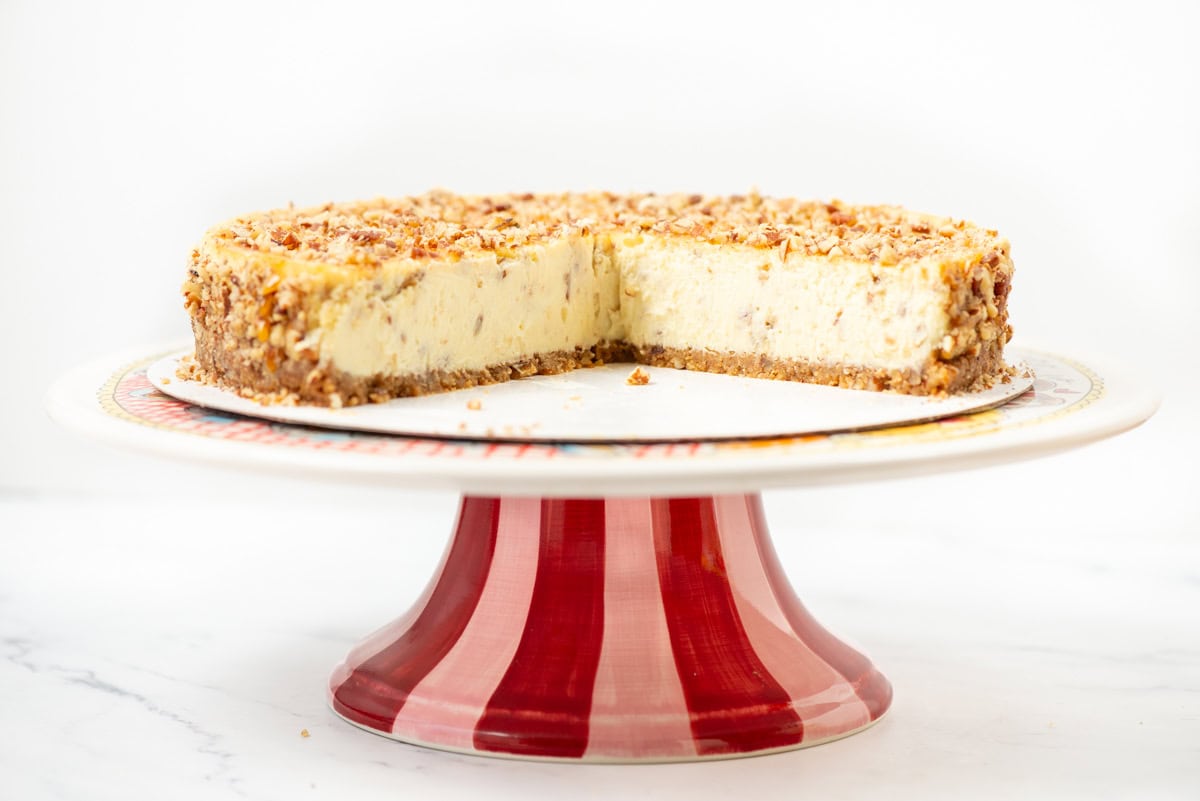 Side view of a cut salted caramel pecan cheesecake where you can see the inside of the cheesecake on a cake stand that's red and pink striped