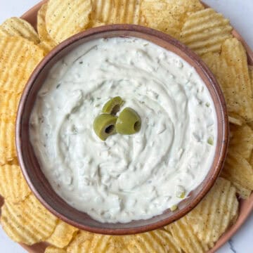 Bowl of dirty martini dip garnished with olives surrounded by kettle chips