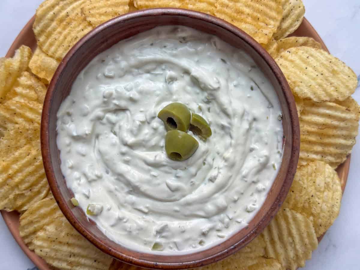 Bowl of dirty martini dip garnished with olives surrounded by kettle chips