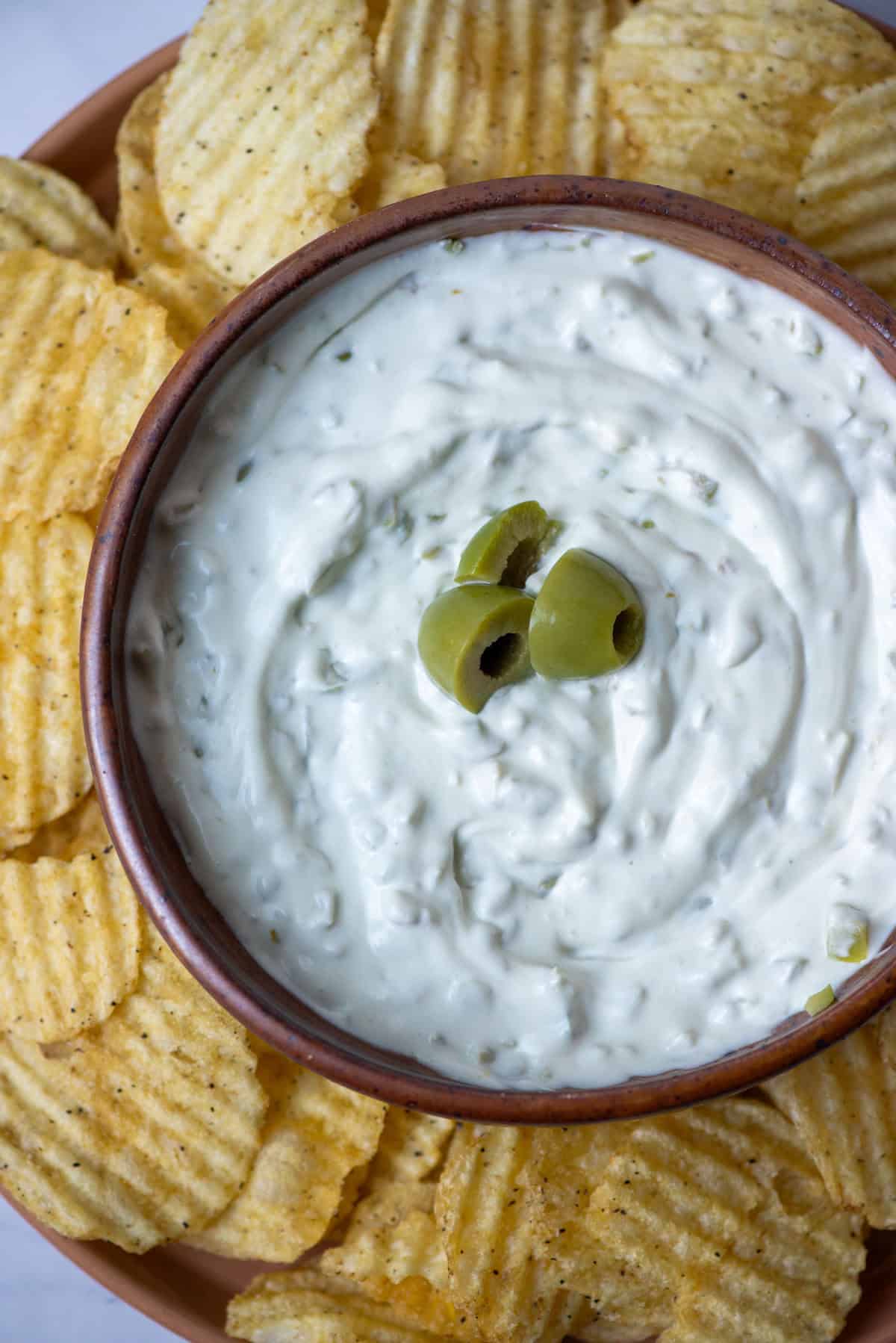 Bowl of dirty martini dip garnished with olives surrounded by kettle chips