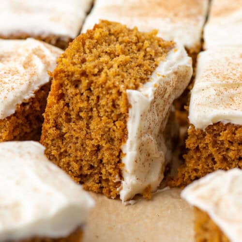 Overhead view of slices of gluten free pumpkin bar cake with cream cheese frosting. The middle slice is turned on its side so that you can see the density and crumb of the cake.
