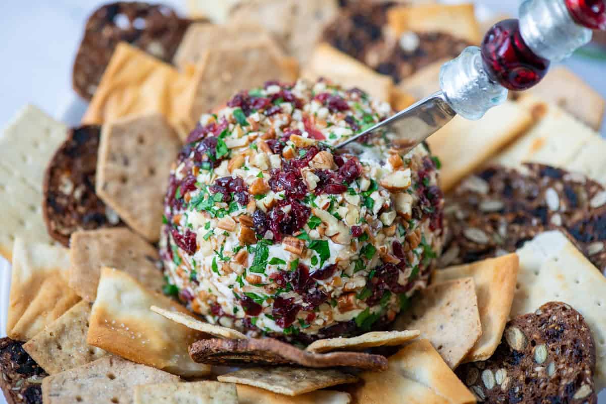 Close up view of cranberry and Pecan crusted cheddar cheese ball surrounded by 4 different types of crackers