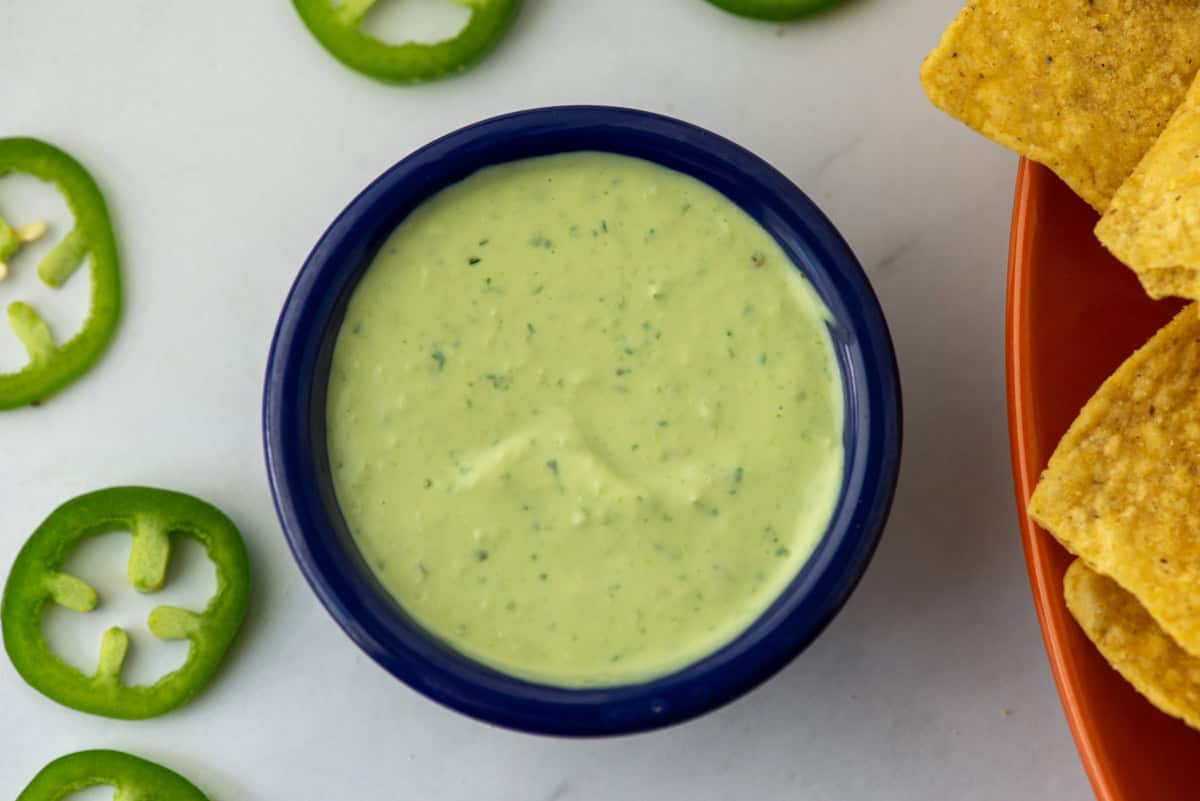 Overhead photo of jalapeño avocado lime crema surrounded by chips and cut jalapeños
