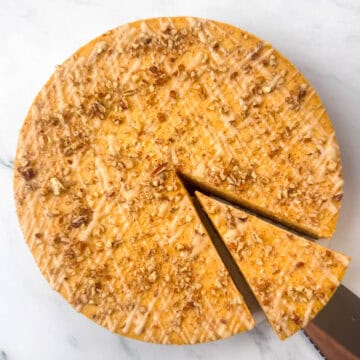 Overhead image of a pumpkin pecan cheesecake where a slice has been cut and it's just starting to be removed with a cake knife