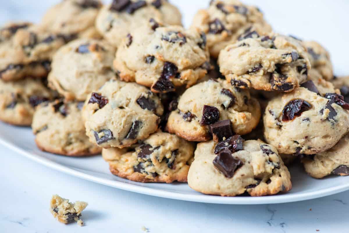 Stacked cherry chocolate chunk cookies on a platter with a few crumbs in front of the platter