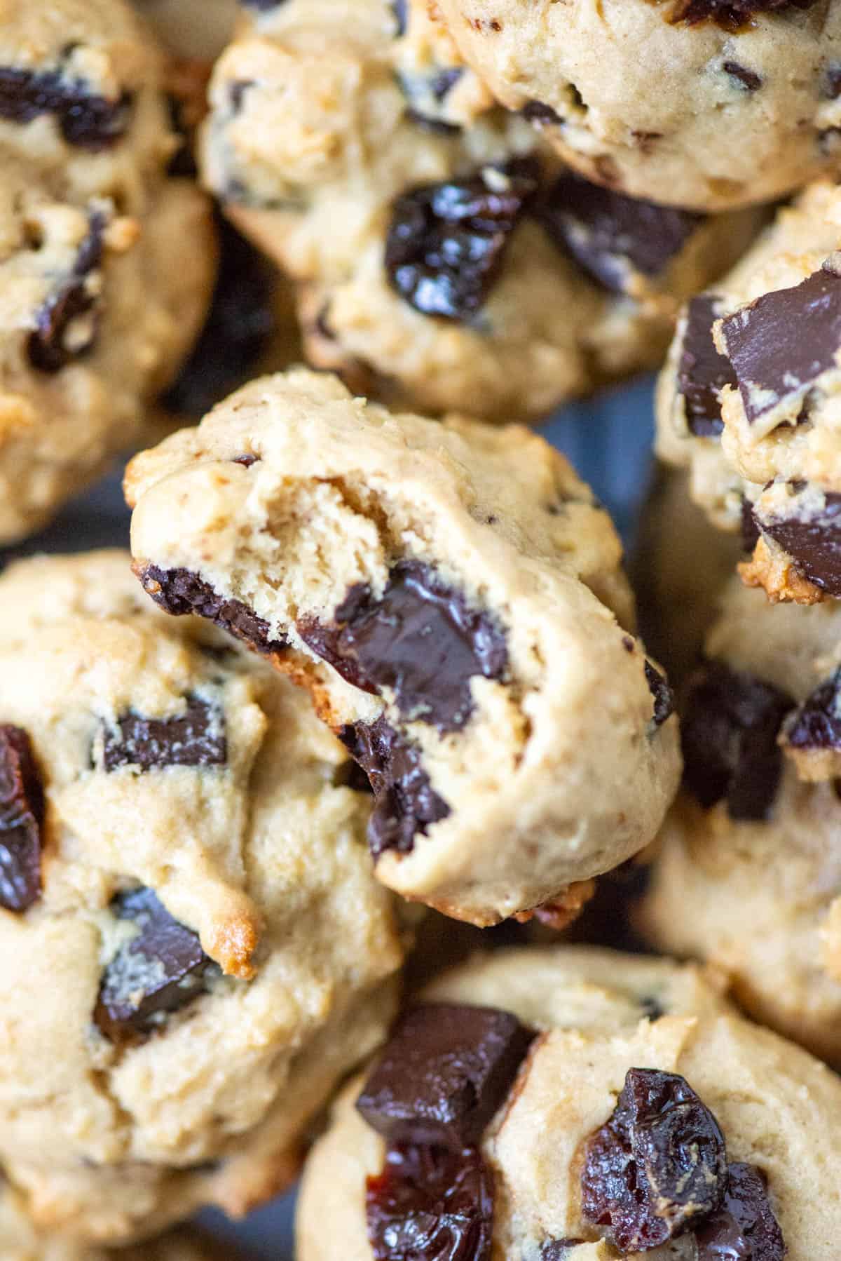 Close up photo of a pile of cherry chocolate chunk cookies with the middle one having a bite taken out