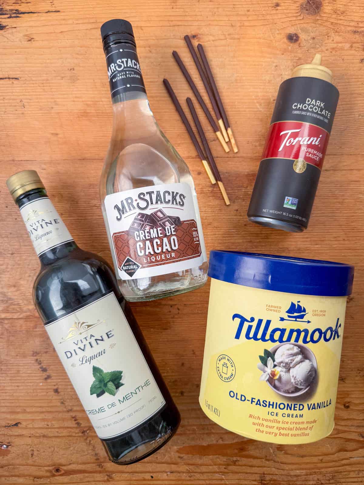 Ingredients needed for a frozen grasshopper cocktail: creme de menthe, white creme de cacao and vanilla ice cream with optional chocolate sauce and Pocky sticks.