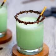 Close up photo of a frozen grasshopper drink made with ice cream in a cocktail glass with a sprinkle rim and a Pocky stick as a stir stick. It has a title overlay that says Frozen Grasshopper Drink and another title overlay that says www.nextlevelbaker.com