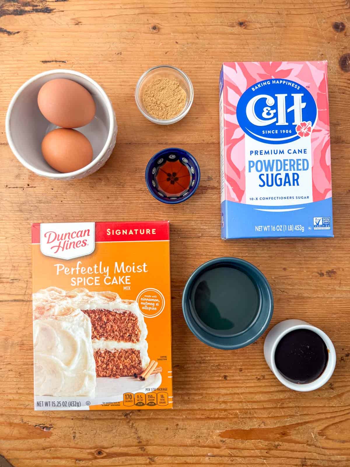 Overhead photo of ingredients needed to make gingerbread crinkle cookies: spice cake mix, molasses, vegetable oil, eggs, ground ginger and vanilla. Then they are highly rolled in white sugar (optional) and powdered sugar.