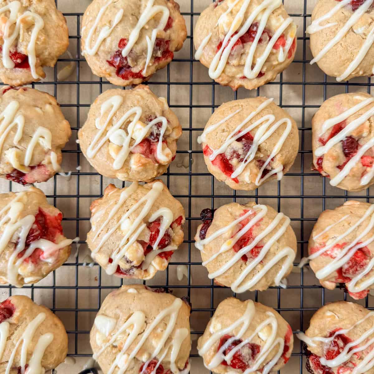 Overhead photo of white chocolate cranberry cookies with an orange drizzle on a wire cooling rack