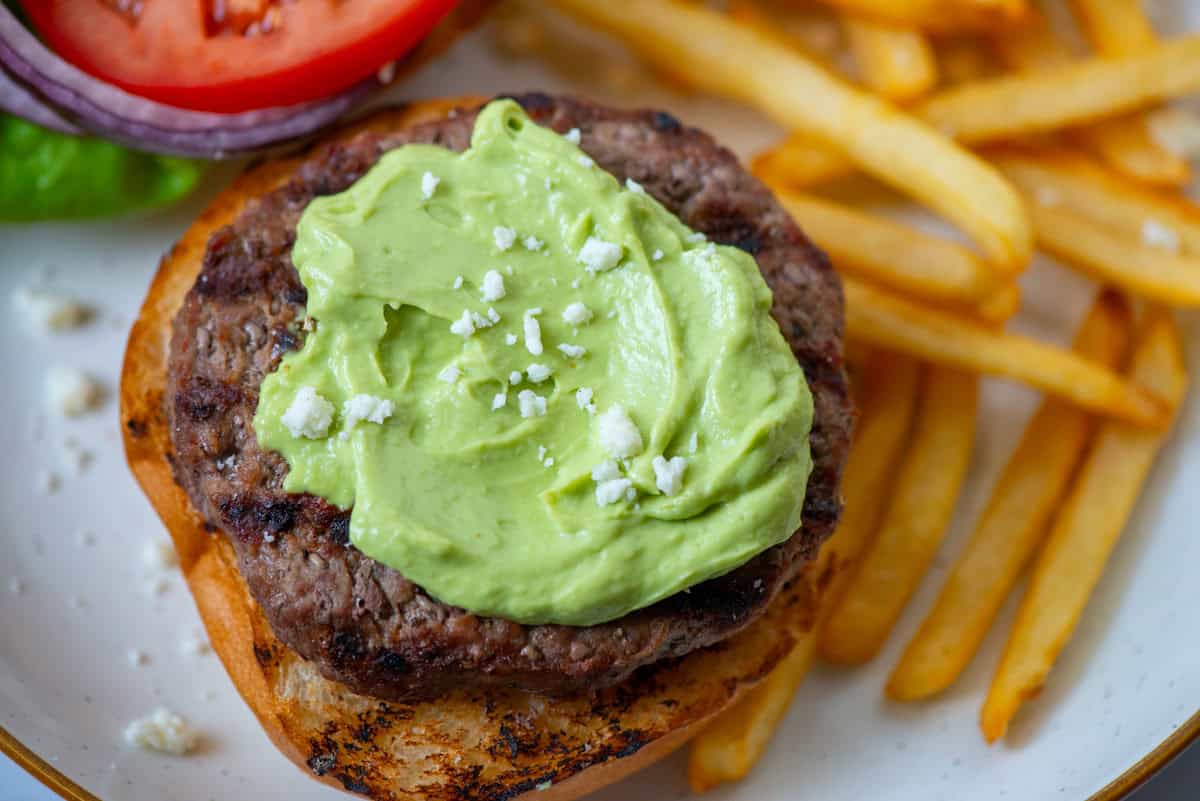 Overhead photo of avocado aioli on a burger with fries and the burger fixings on the side