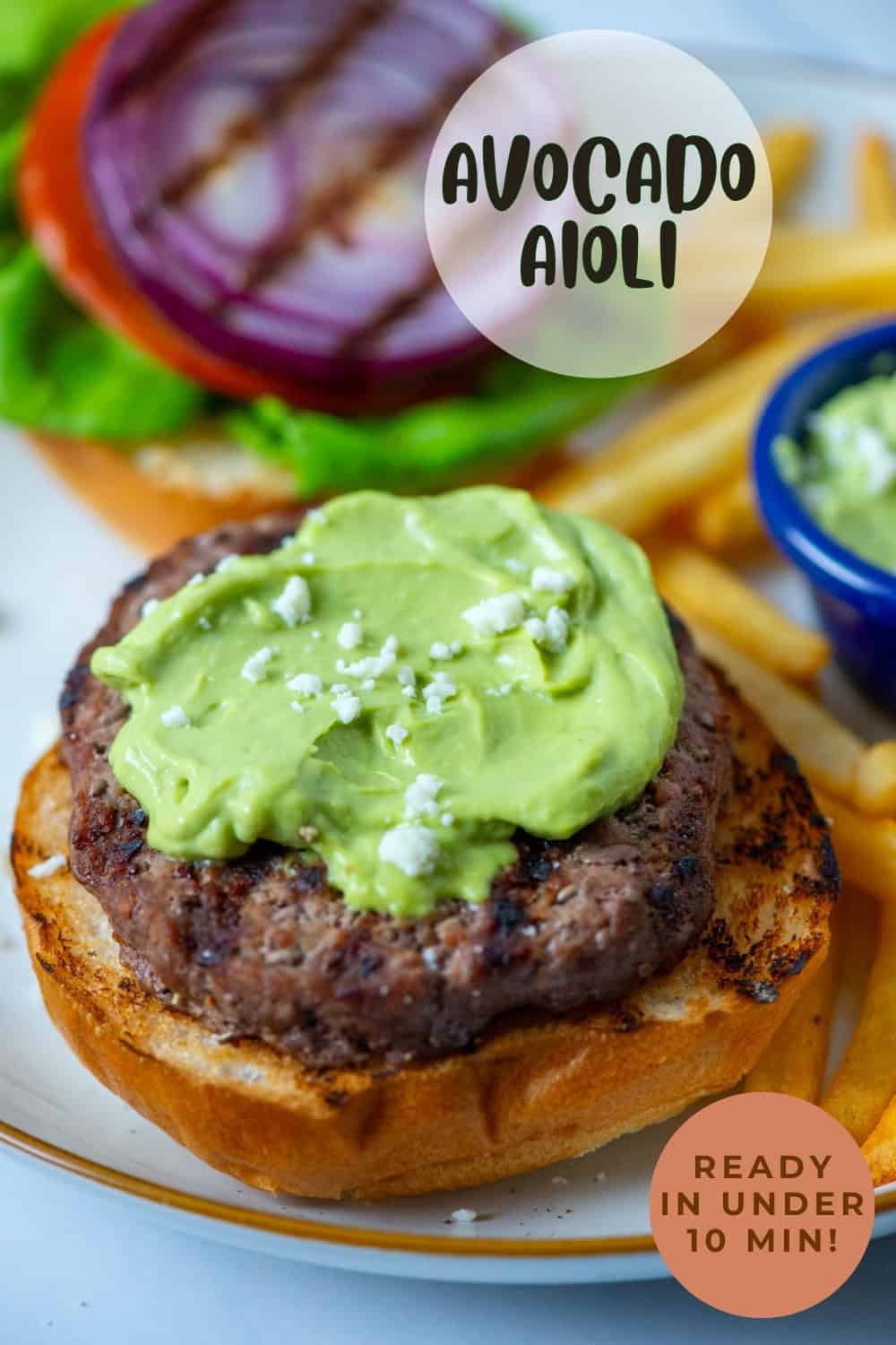 Overhead angled view of open face burger topped with avocado aioli surrounded by fries, the burger toppings and a partial view of a condiment cup filled with avocado aioli with a title overlay that says Avocado Aioli and another overlay that says Ready in Under 10 Min!