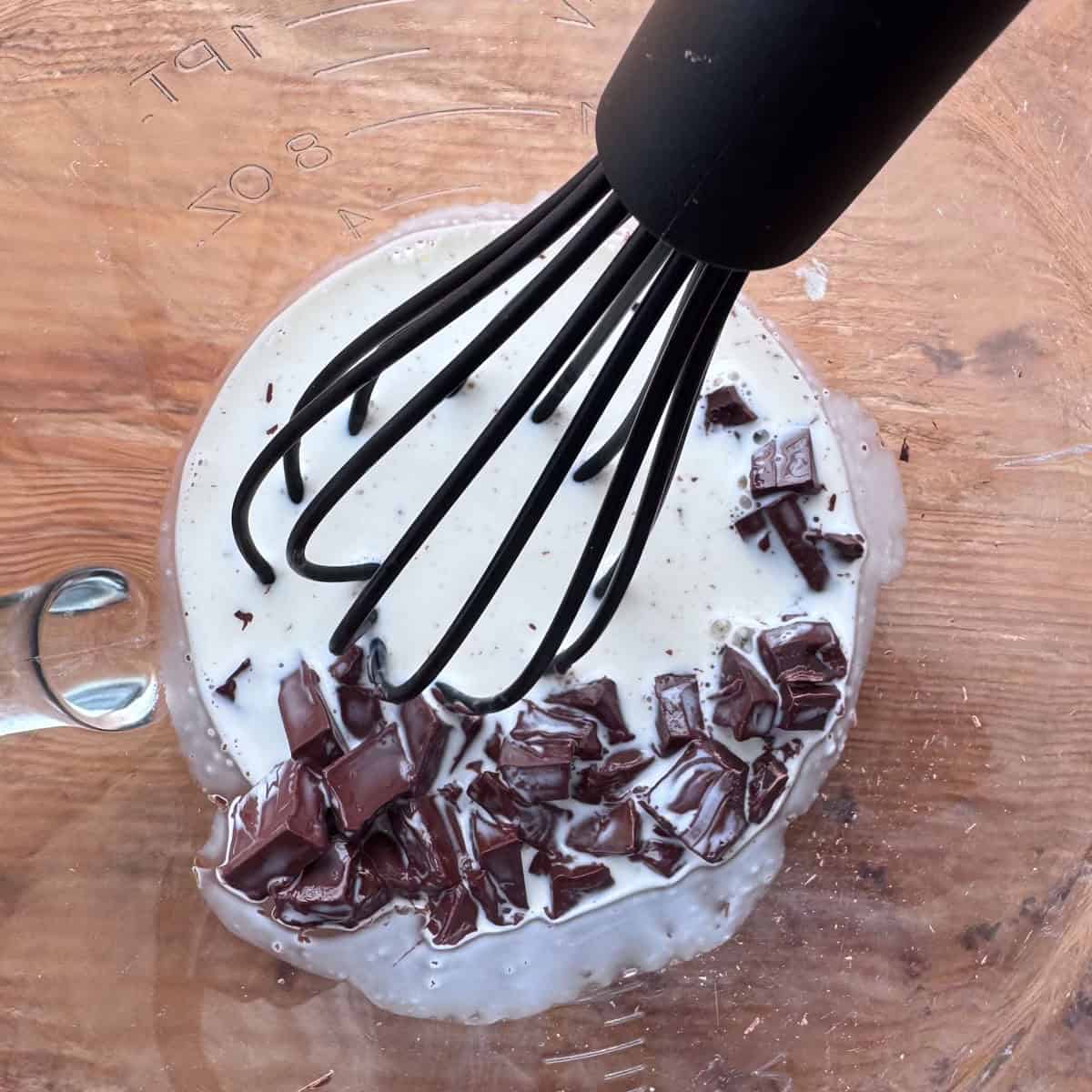 Photo illustrating second step of making ganache: hot heavy whipping cream poured over the rough chopped chocolate and orange extract