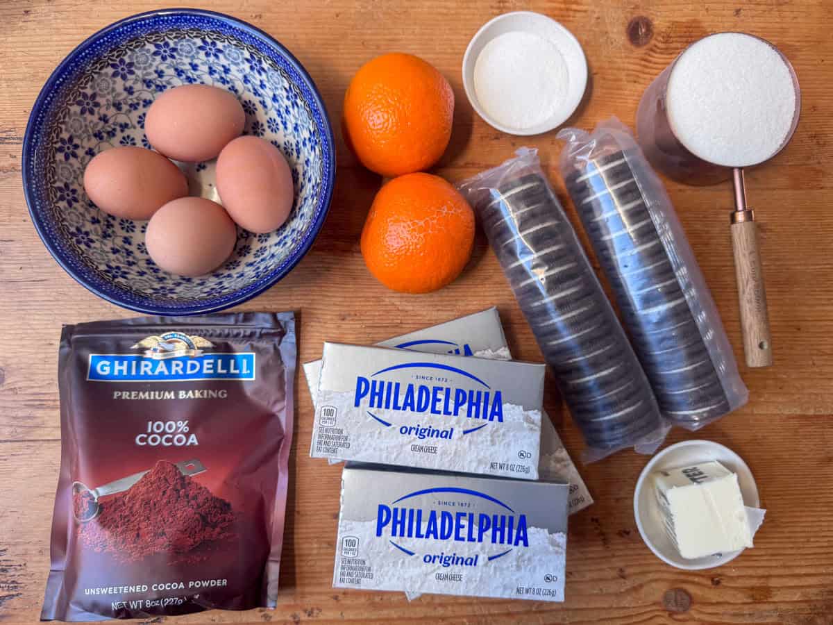 Ingredients needed for chocolate orange cheesecake: chocolate sandwich cookies, salted butter, white sugar, cream cheese, eggs, cocoa powder and oranges