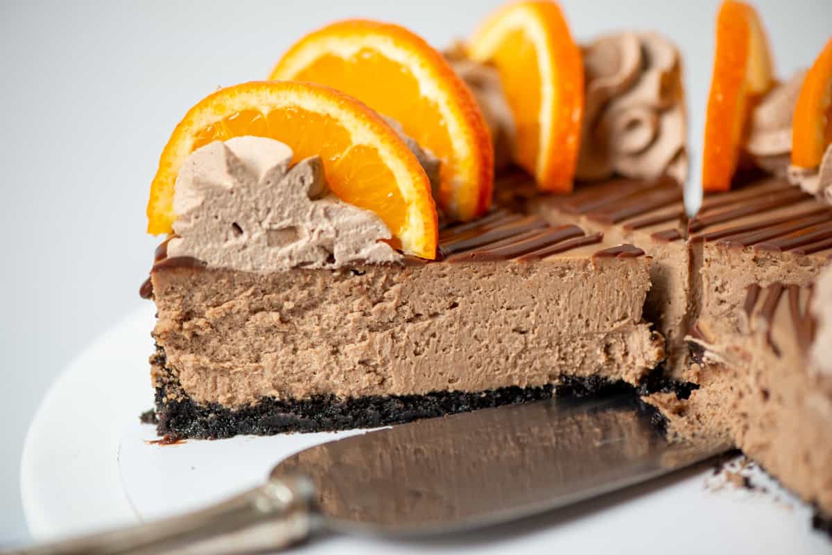 Side view of a orange chocolate cheesecake on a serving plate next to a serving knife