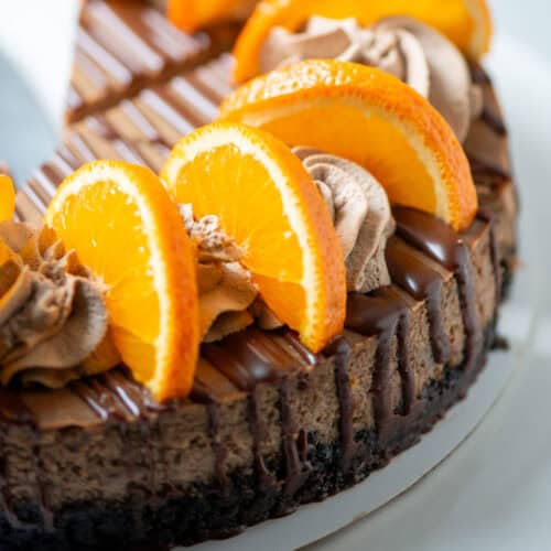 Partial view of an orange chocolate cheesecake garnished with orange chocolate ganache and orange slices