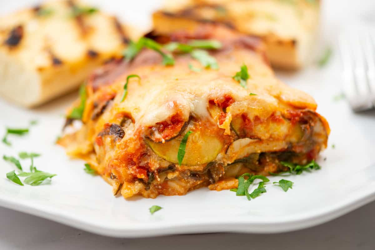 Side view of a piece of lasagna on a small plate with grilled garlic bread