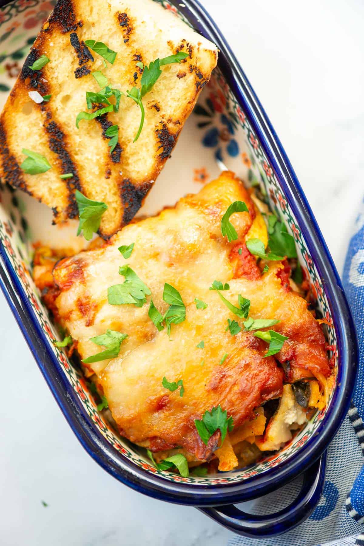 A piece of lasagna in a small ceramic bowl with grilled garlic bread