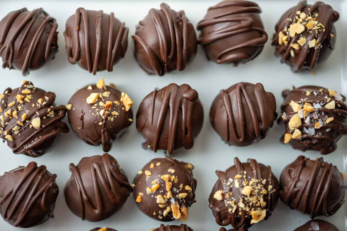Overhead close up photo of chocolate peanut butter truffles on a plate, some are decorated with crushed peanuts and the rest are decorated with chocolate drizzle