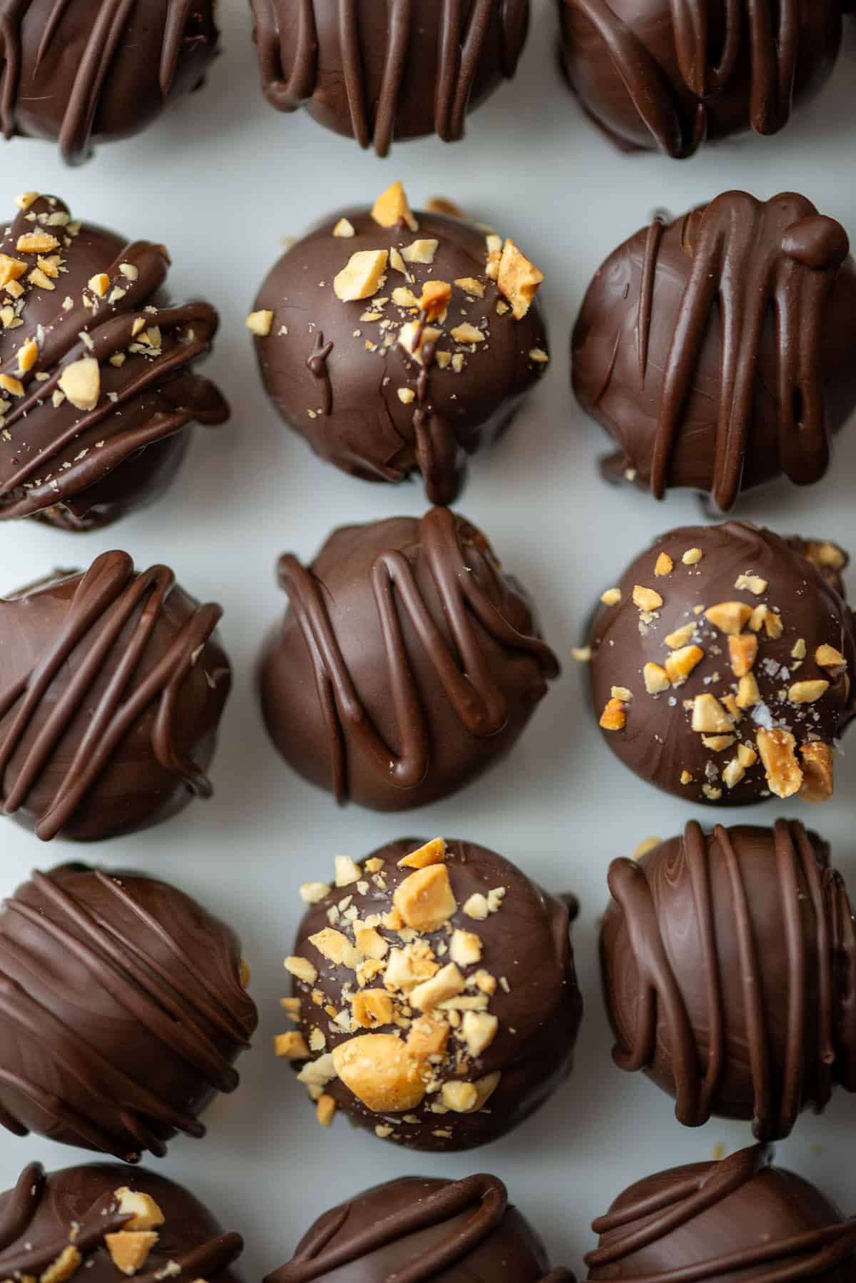 Overhead close up photo of chocolate peanut butter truffles on a plate, some are decorated with crushed peanuts and the rest are decorated with chocolate drizzle