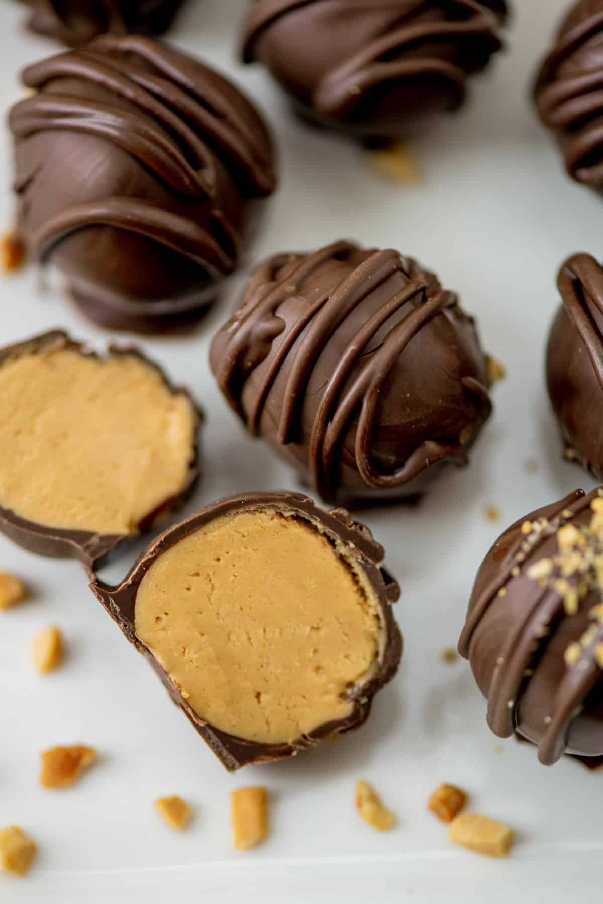 Overhead photo of chocolate peanut butter truffles with one cut in front so that you can see the inside with crushed peanuts sprinkled in the foreground