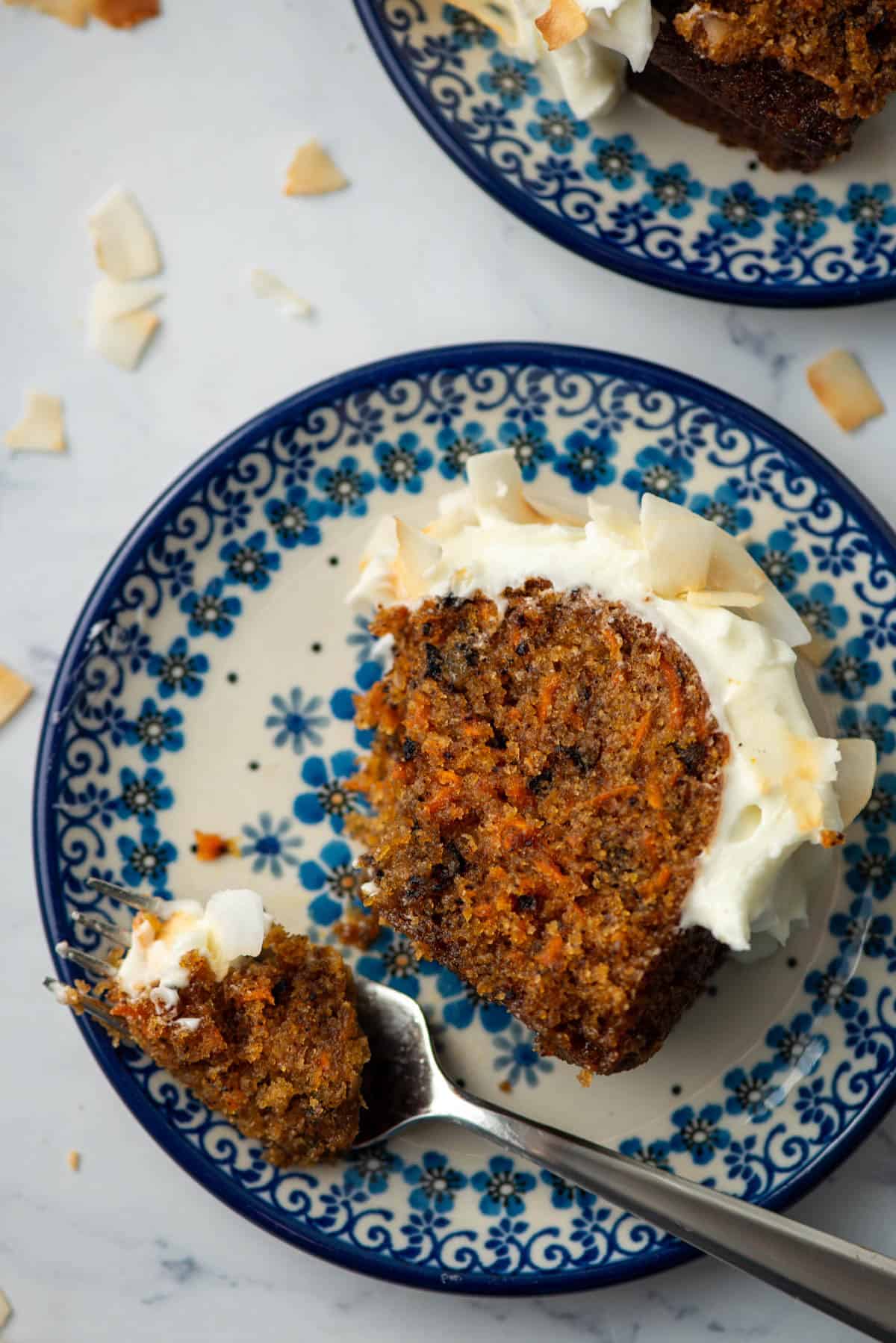 Overhead view of a slice of carrot bundt cake on a plate with a bite on a fork with another slice on a plate in the background