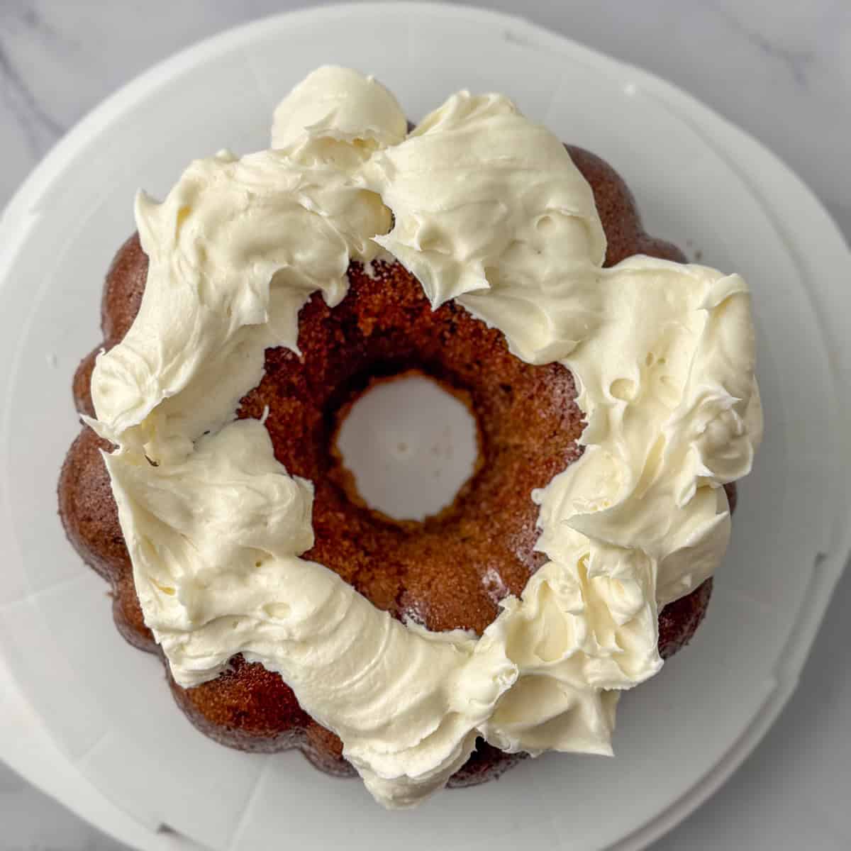 Step one in decorating a carrot bundt cake: add the frosting to the top of the cake in globs