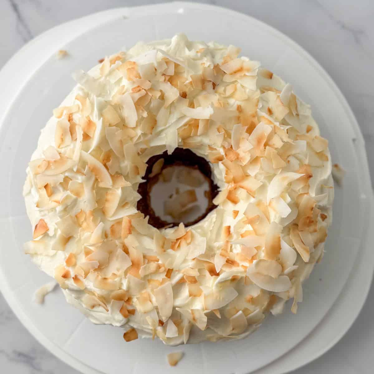 Step four in decorating a carrot bundt cake: toast and add the toasted coconut to the top of the frosted cake