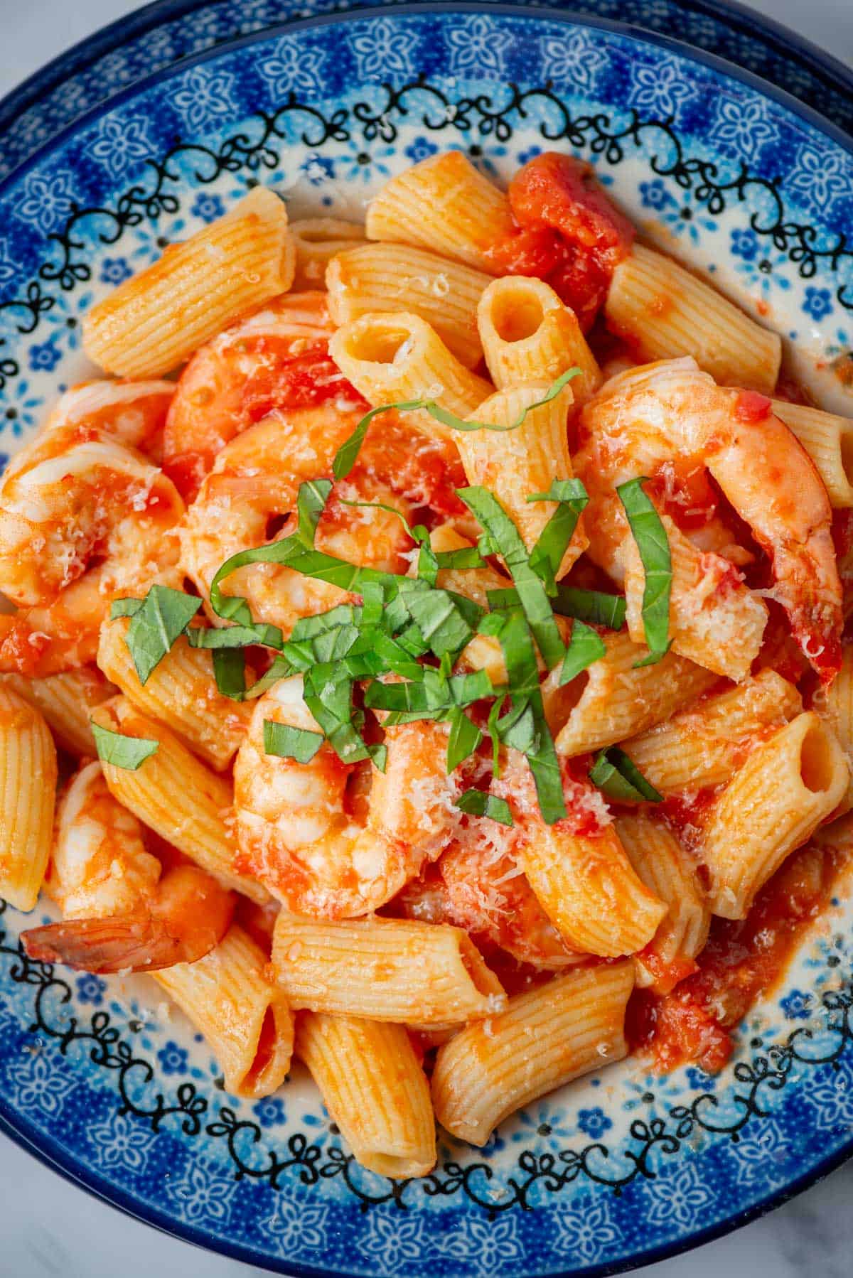 Overhead view of shrimp rigatoni with tomato butter sauce topped with parmesan cheese and a basil garnish with more basil in the background.