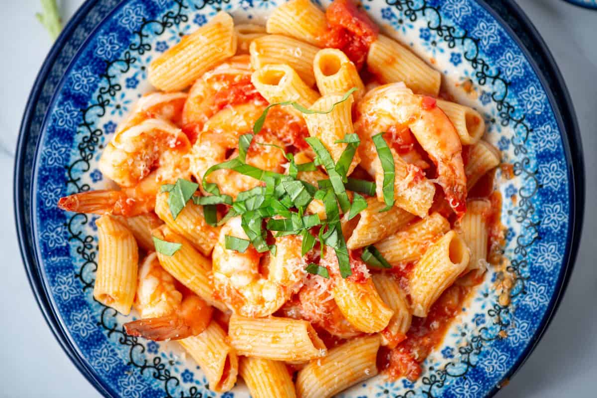 Overhead close up view of shrimp rigatoni garnished with small, thin strips of basil on a blue plate