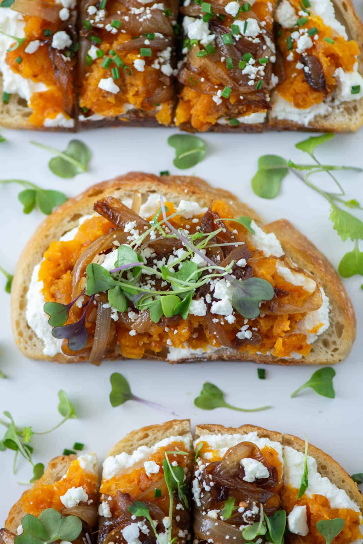 Overhead view of three pieces of squash toast. the center piece is not cut. Both the top and bottom pieces are sliced in quarters. This is illustrating the different ways to cut the toast. If you cut it one way, it's a meal. If you cut it another way, it's an appetizer.