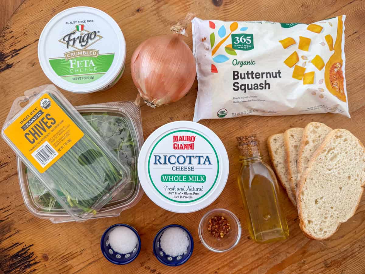 Ingredients needed for squash toast: butternut squash, onion, ricotta cheese, feta cheese, olive oil, salt, crushed red peppers, micro greens and/or chives and bread.