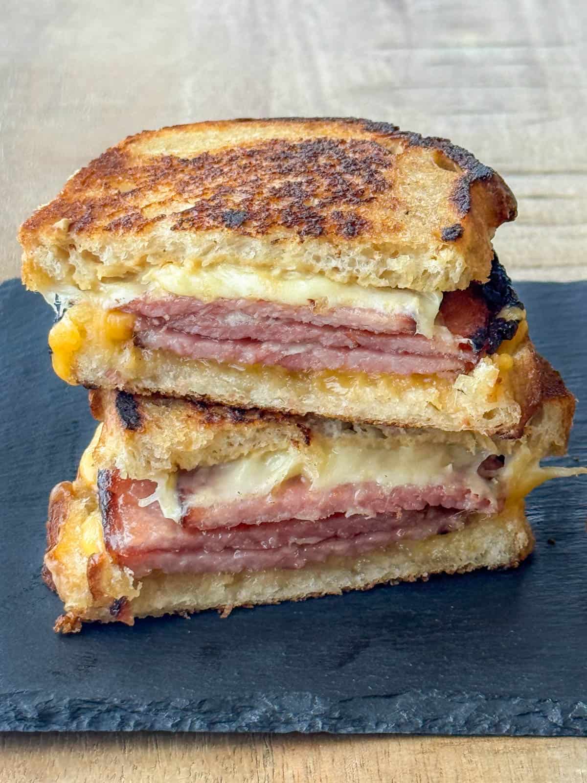 Side view photo of a grilled ham and cheese sandwich that's been cut in half and stacked on top of each other