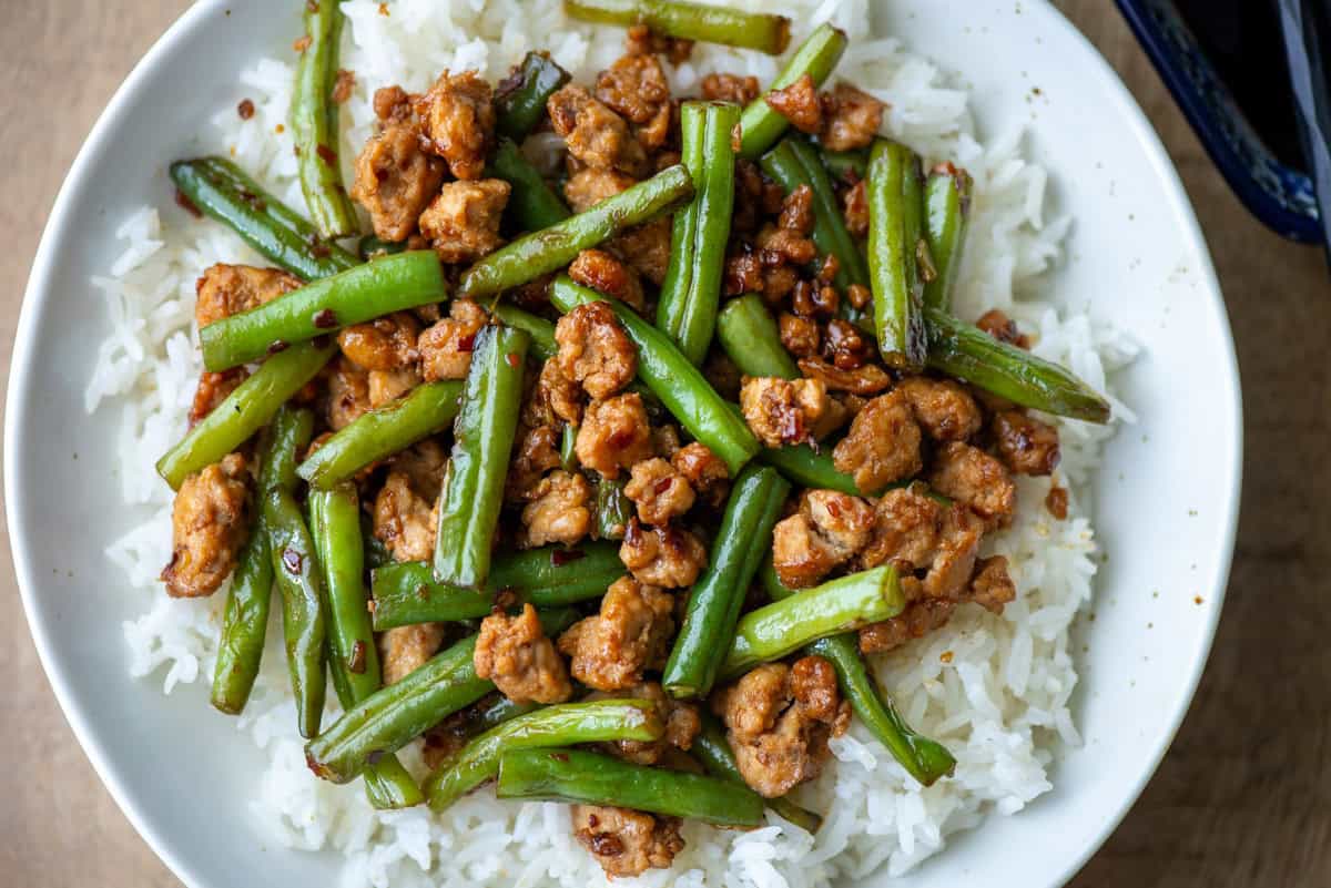 Overhead photo of a partial plate of ground chicken stir fry with green over white jasmine rice with a small bowl of soy sauce partially visible to the side
