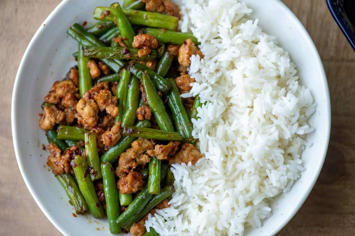 Overhead view of a plate of ground chicken stir fry with green beans on one side and white jasmine rice on the other