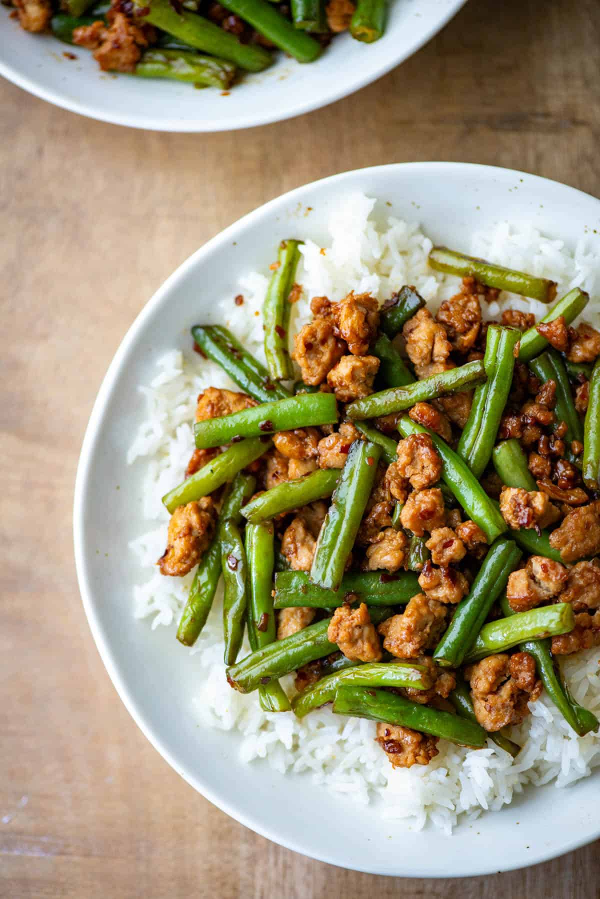 Overhead photo of a partial plate of ground chicken stir fry with green over white jasmine rice with another bowl partially visible in the background