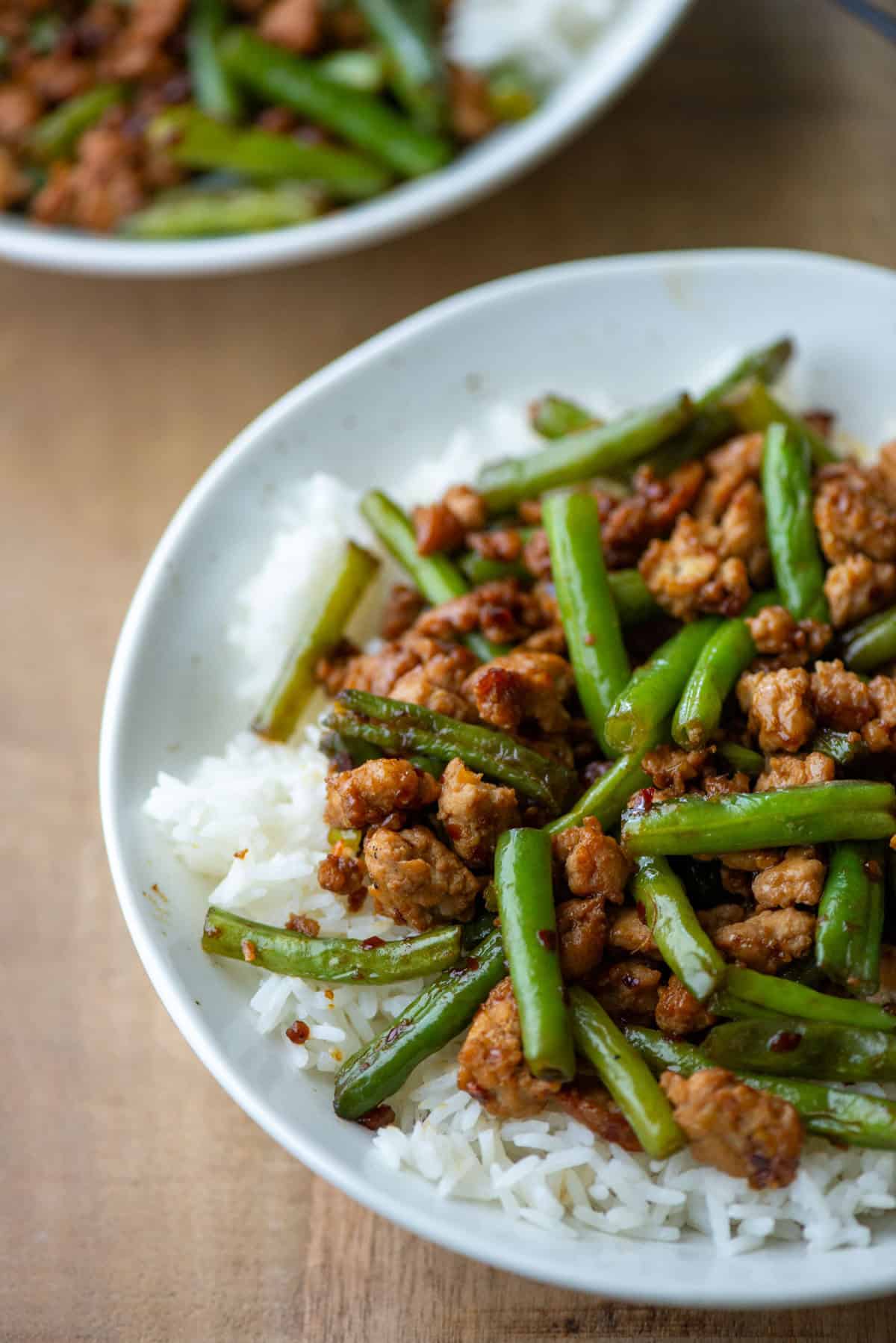 Overhead view of a partial plate of ground chicken stir fry with green over white jasmine rice with another bowl partially visible in the background