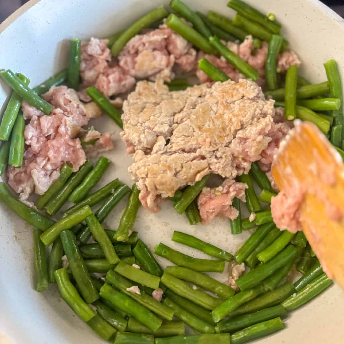 Step two of making ground chicken stirfry: showing the ground chicken cooking with the beans in sesame oil