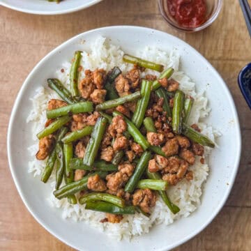 Overhead photo of ground chicken stir fry with green beans and rice and a side of Gochujang on the side