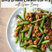 Overhead view of a partial plate of ground chicken stir fry with green over white jasmine rice with another bowl partially visible in the background with a title overlay that says Spicy Ground Chicken Stir Fry with Green Beans and another title overlay that says Quick 30 Min Meal