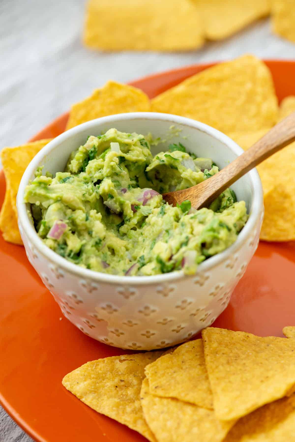 Guacamole in a bowl surrounded by chips on an orange plate