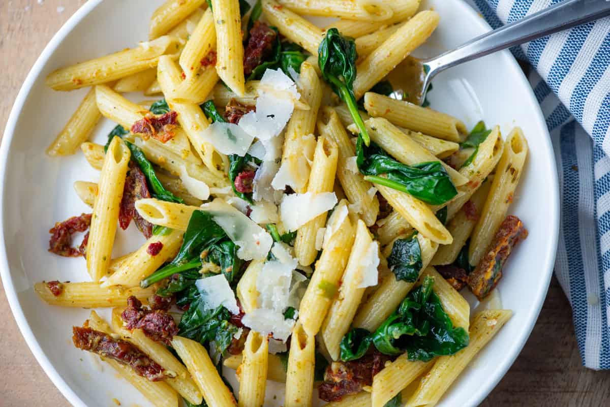 Overhead photo of pasta pesto with sun-dried tomatoes on a plate with a fork sticking out and a napkin to the side