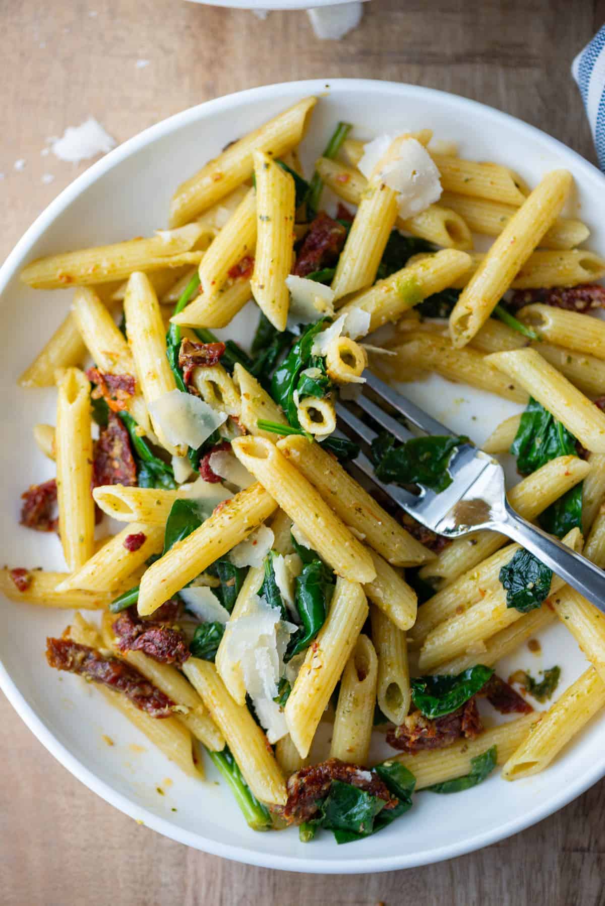 Overhead partial photo of pasta pesto with sun-dried tomatoes with a fork in the middle