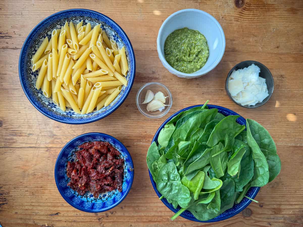 Ingredients needed to make pesto pasta with sun dried tomatoes: penne or pasta of choice, pesto, sun dried tomatoes, garlic and spinach