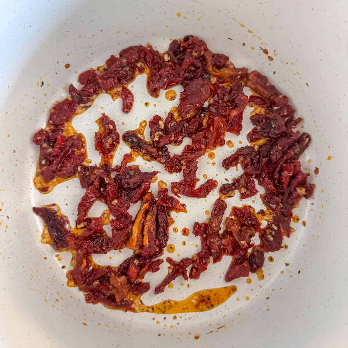 Sun-dried tomatoes cooking in a pot with garlic